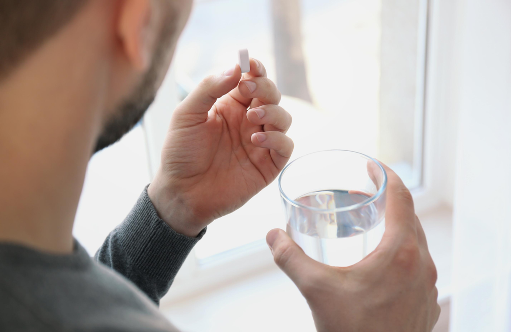 Africa Studio/Shutterstock.com A person taking a white pill holding a glass of water.